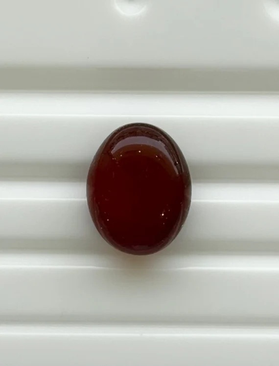 A dark red oval bead resting on a white ribbed surface.