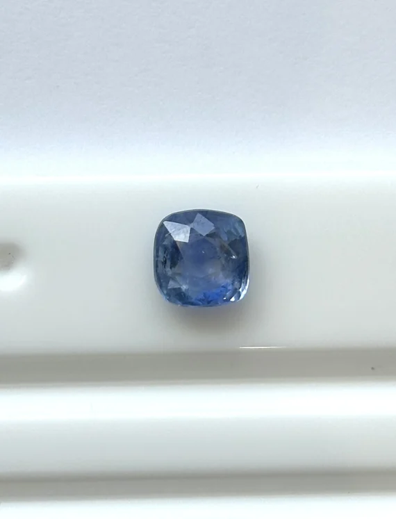 A cushion-cut blue gemstone placed on a white surface