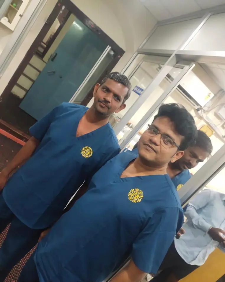 Three medical staff in blue scrubs pose in a clinic hallway near glass doors, with Rotary logos on their chests.