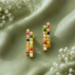 Gold earrings with square multicolor gems and small diamonds on a green satin background, elegant and sparkling.