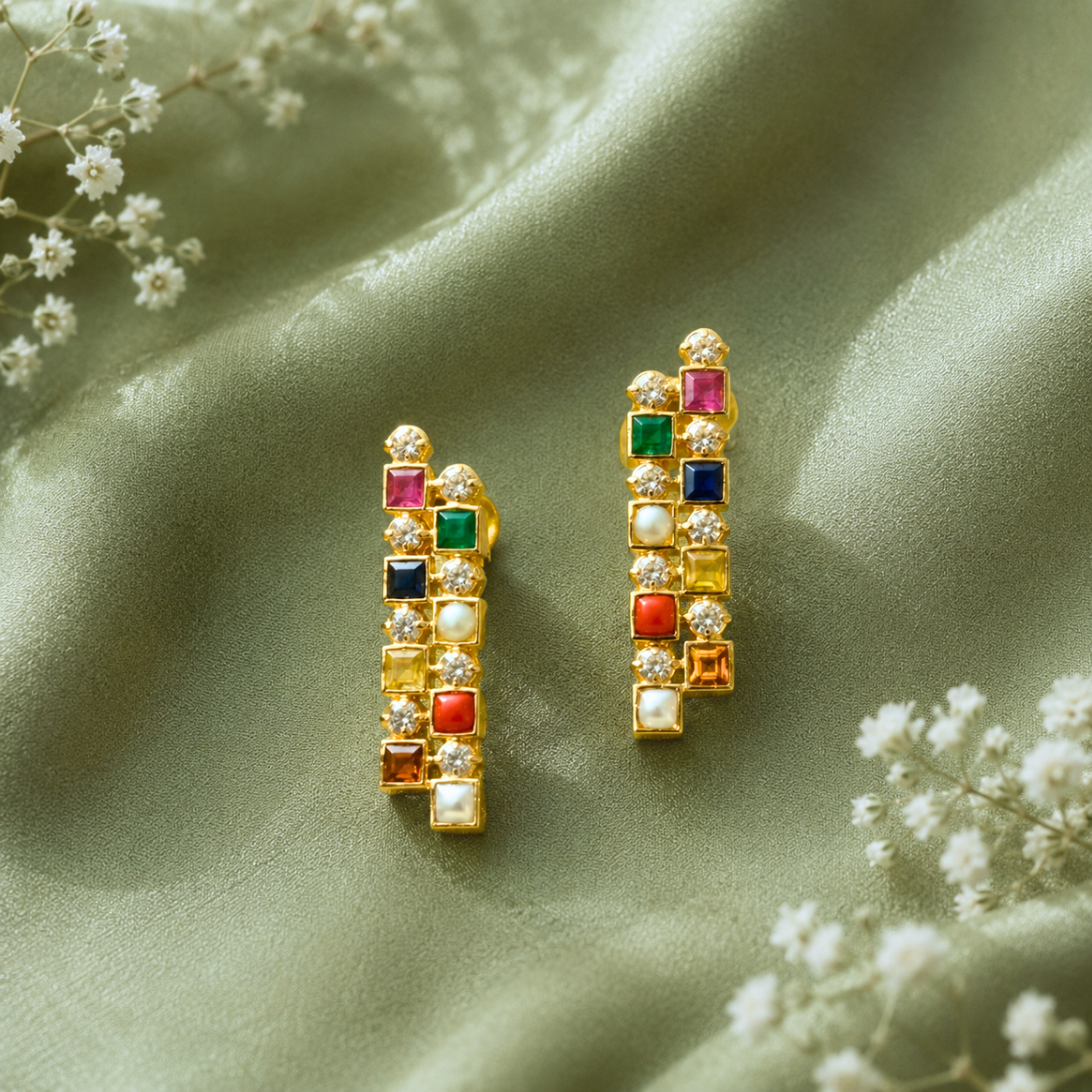 Gold earrings with square multicolor gems and small diamonds on a green satin background, elegant and sparkling.