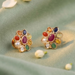 Gold-tone flower-shaped earrings with multicolored gemstones on green fabric.