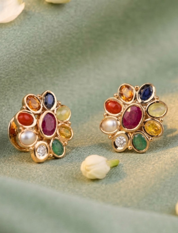 Gold-tone flower-shaped earrings with multicolored gemstones on green fabric.