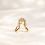 Gold ring with a curved halo setting studded with diamonds, resting on a reflective surface.