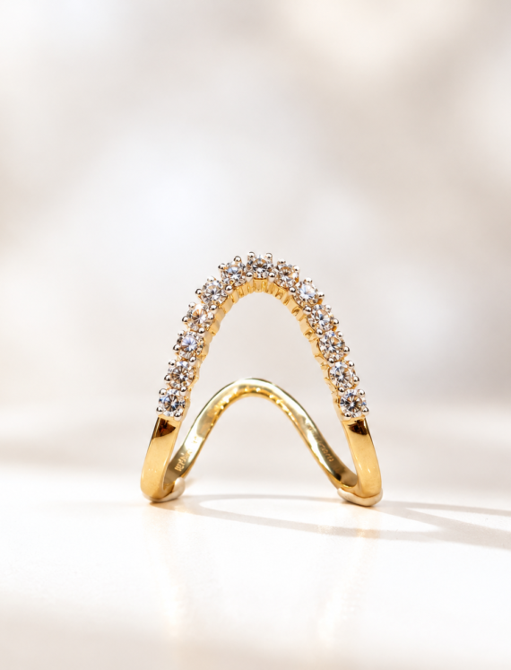 Gold curved diamond ring standing on a white surface, pavé-set stones along the arch, elegant jewelry piece.