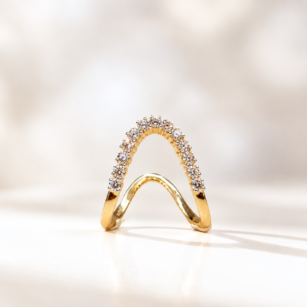 Gold curved diamond ring standing on a white surface, pavé-set stones along the arch, elegant jewelry piece.