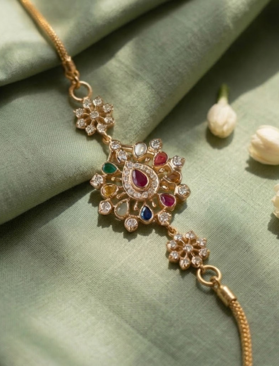 Gold-tone bracelet with a central flower-shaped pendant encrusted with small diamonds and multicolored gemstones on a green fabric backdrop.