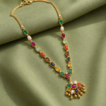 Gold necklace with a multicolored gemstone pendant laid on green satin fabric.
