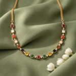 Gold necklace with square multicolor gemstones and diamond accents on green fabric background.