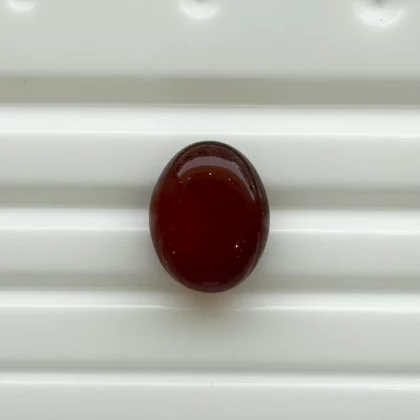 A dark red oval bead resting on a white ribbed surface.