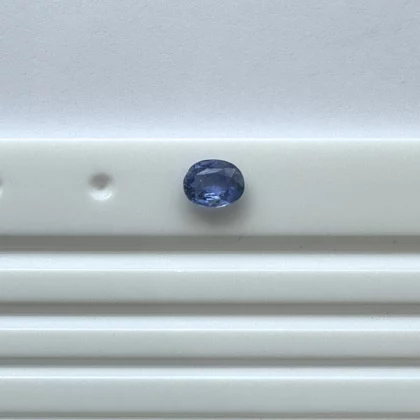 Blue faceted gemstone resting on a pale gray, grooved metal surface.