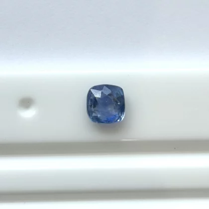 A cushion-cut blue gemstone placed on a white surface, showcasing its faceted facets and rich color.