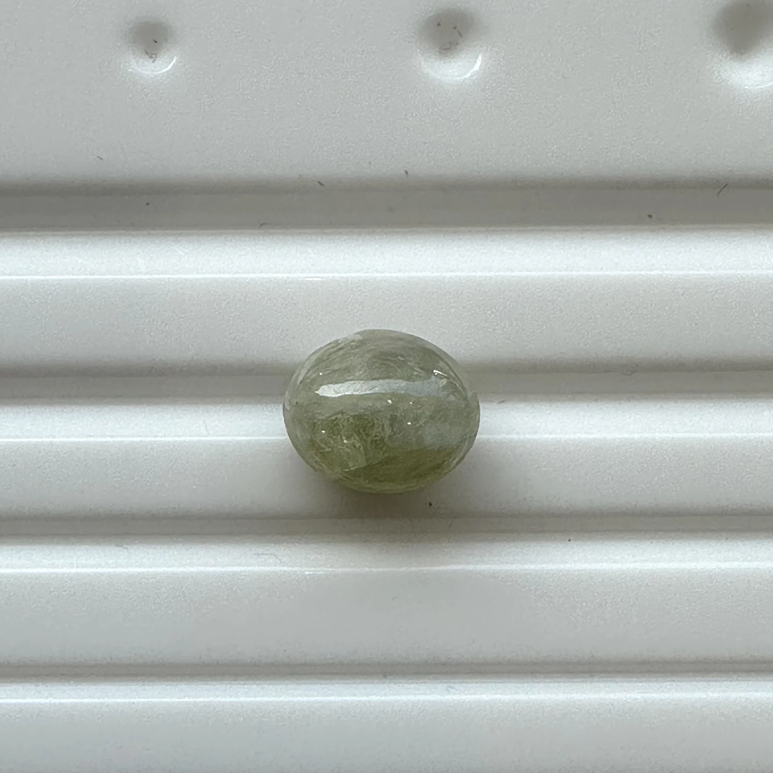 cats eye 189-35258 - N Gopaldaas Jewellers A small mossy-green marble resting on a light gray metal shelf.